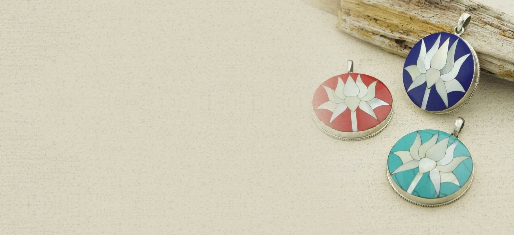 Three sterling silver lotus pendants with mother-of-pearl inlay on lapis, coral and turquoise, resting against driftwood