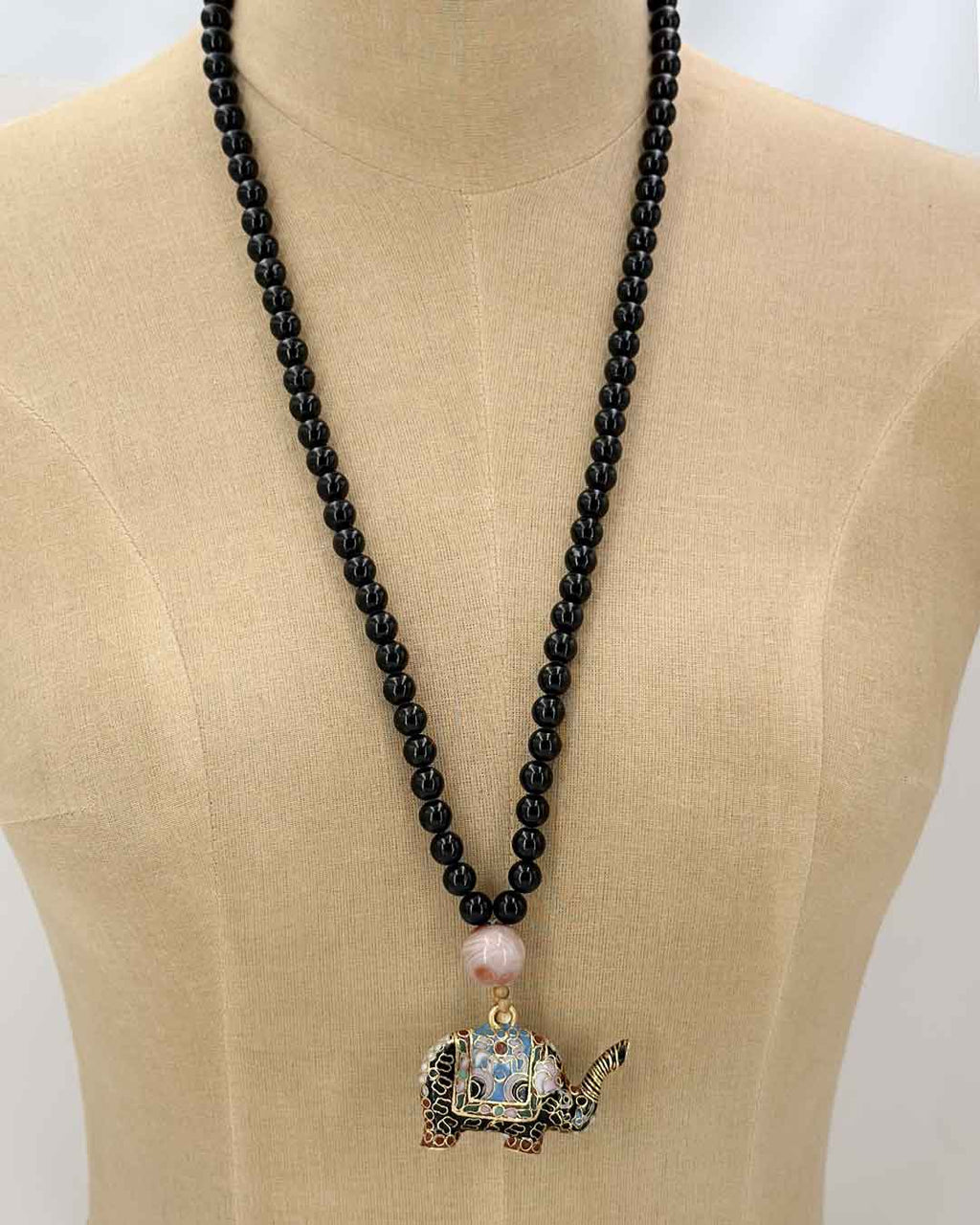 Black stone bead necklace with cloisonne elephant pendant displayed on a dress form mannequin, showing drape and pendant placement