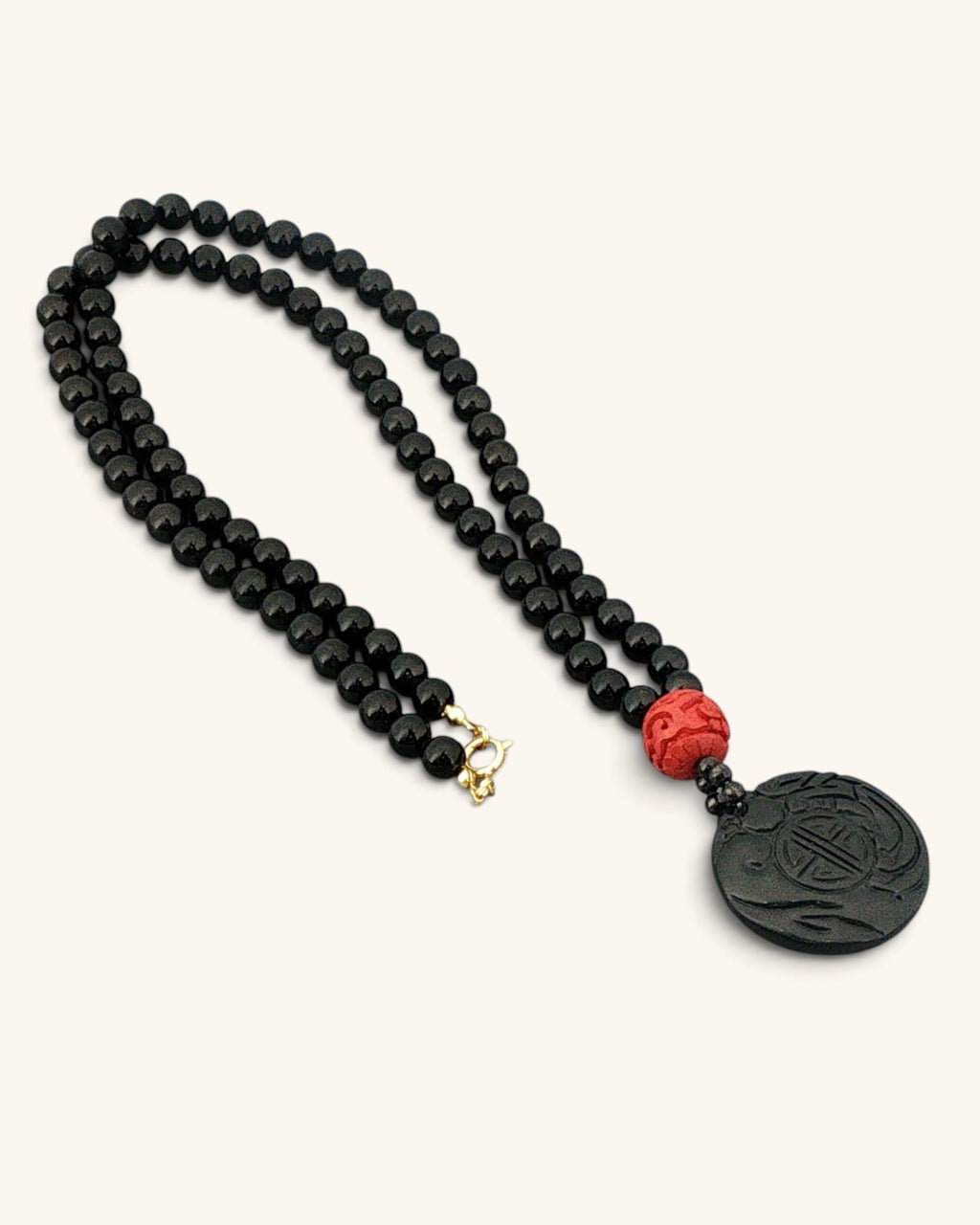 Black stone bead necklace laid flat on white, full 29 inch strand with the carved black jade disc pendant