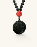 Close view of the carved black jade disc pendant with a red carved bead above it on black stone beads