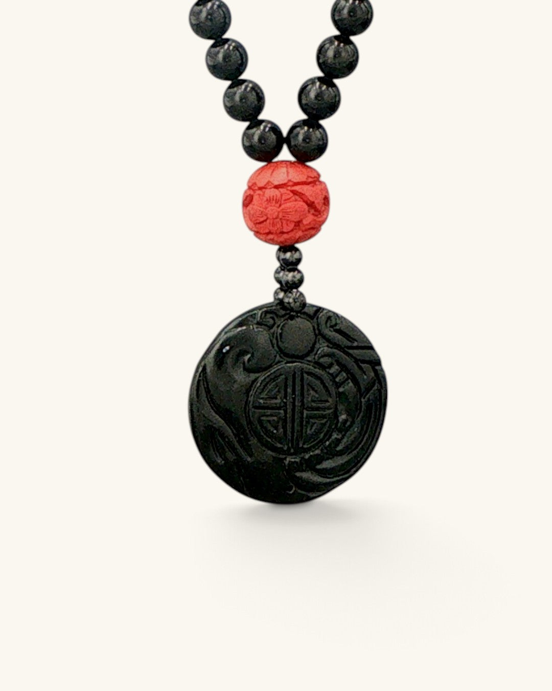 Close view of the carved black jade disc pendant with a red carved bead above it on black stone beads