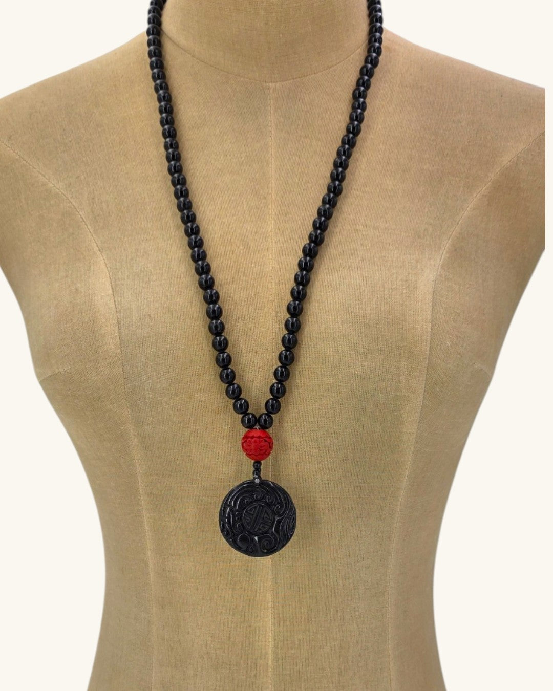 Black stone bead necklace with carved black jade disc pendant shown long on a linen dress form