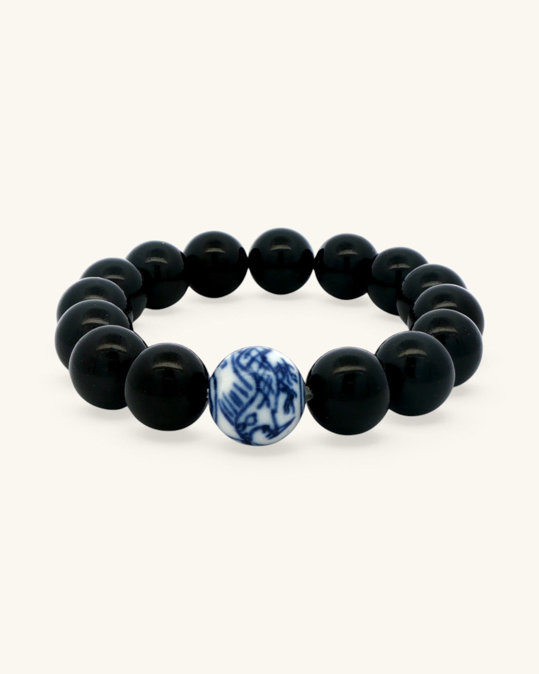 Close view of the blue and white porcelain bead set among glossy black obsidian beads on the stretch bracelet