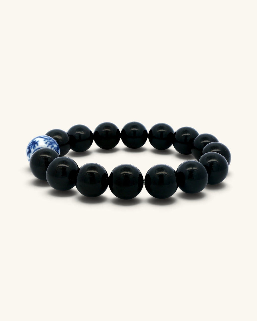 Black obsidian bead bracelet standing upright, side view with the blue and white porcelain bead to the left