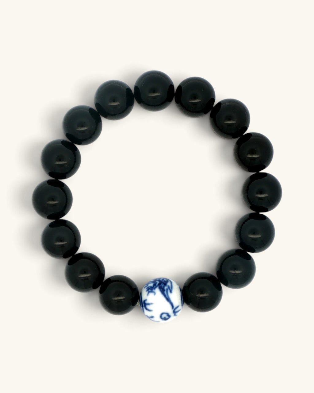 Black obsidian bead bracelet laid flat in a circle, the blue and white porcelain bead at the bottom edge
