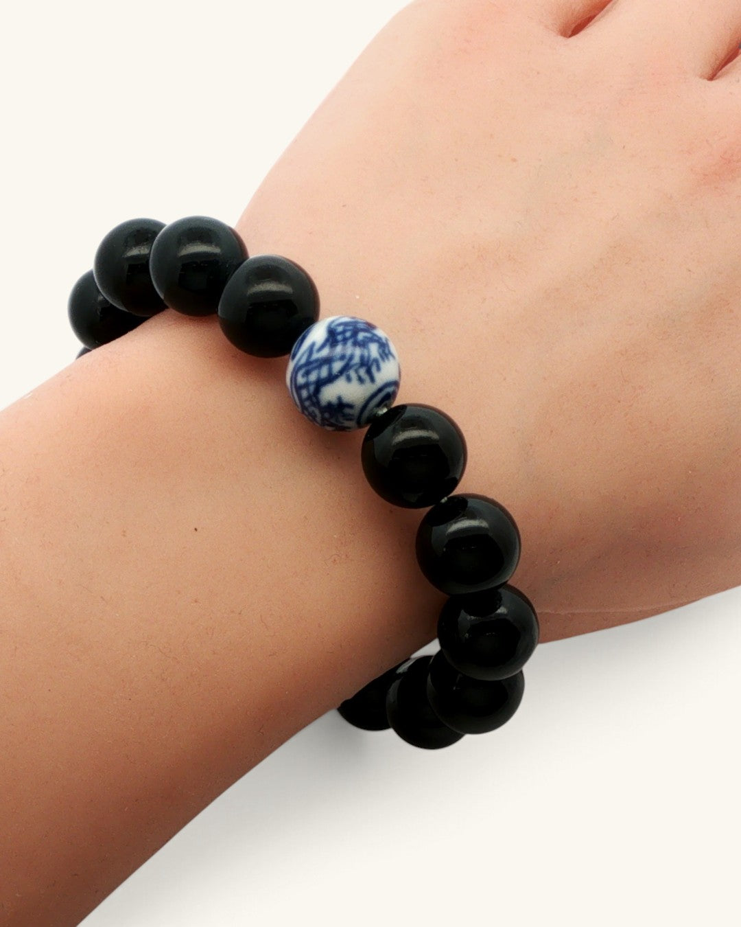 Black obsidian bead bracelet with one blue and white porcelain bead, worn on a wrist, seen from above