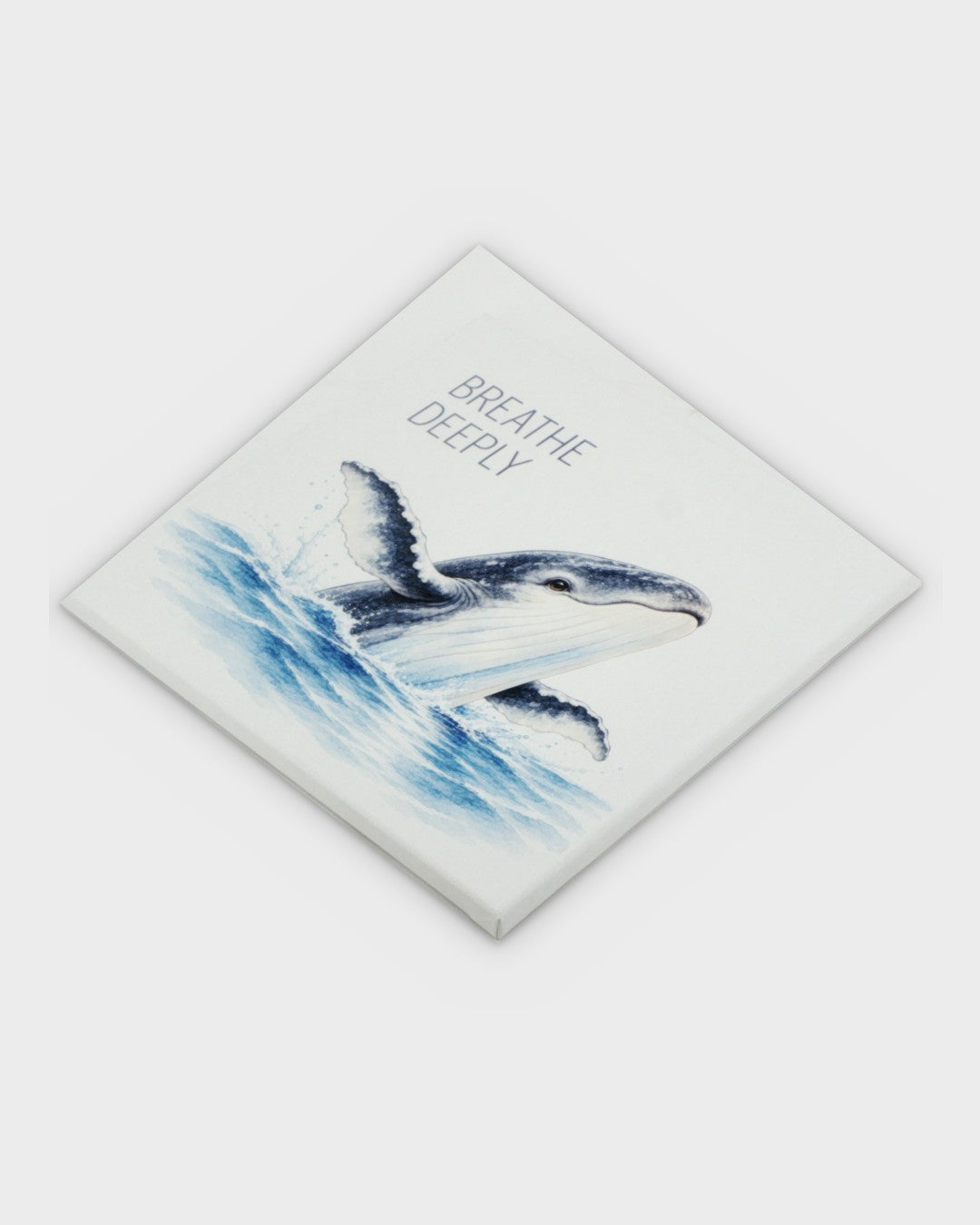 Breathe Deeply watercolor whale canvas wall art tilted at a diagonal angle, showing the full canvas with breaching humpback whale and ocean waves