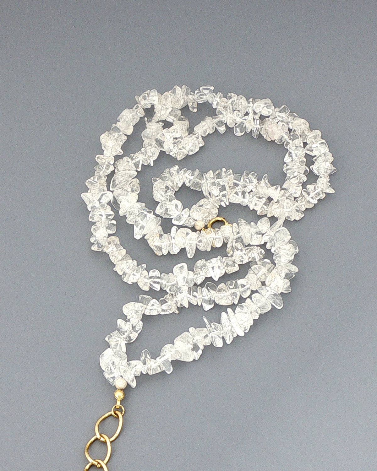 Close view of tumbled clear quartz chips on the double strand necklace, coiled on grey with the gold clasp