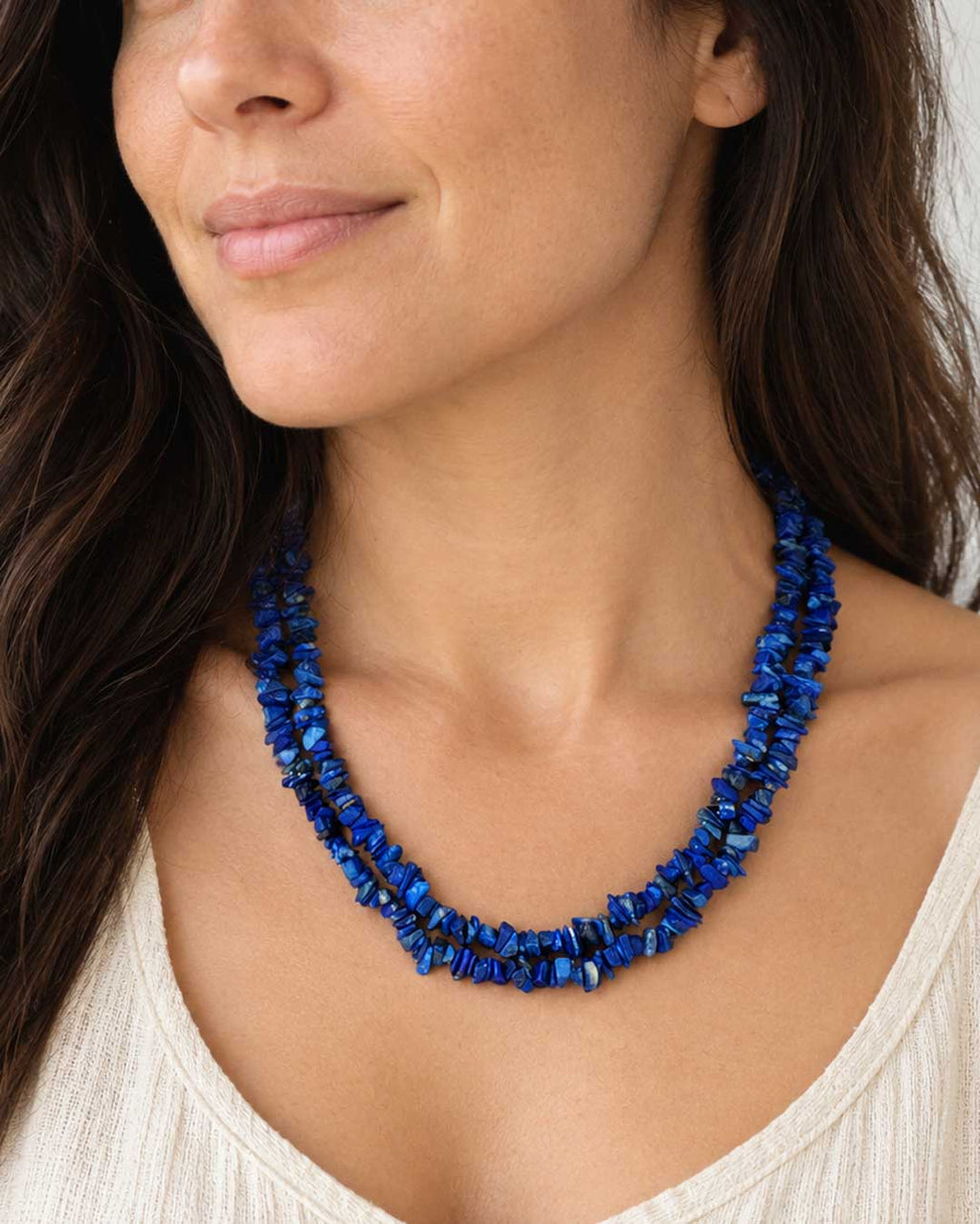 Lapis lazuli chip double strand necklace worn over a white top, deep blue chips at the collarbone on a model