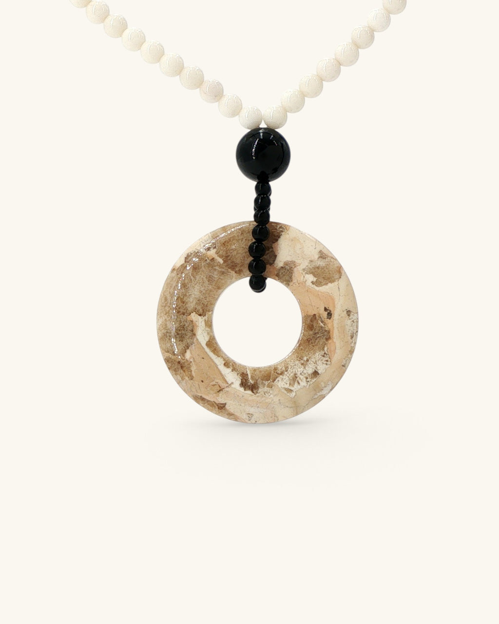 Brown jasper donut pendant at an angle showing its sandstone-like pattern, mother of pearl beads above