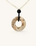 Brown jasper donut pendant at an angle showing its sandstone-like pattern, mother of pearl beads above