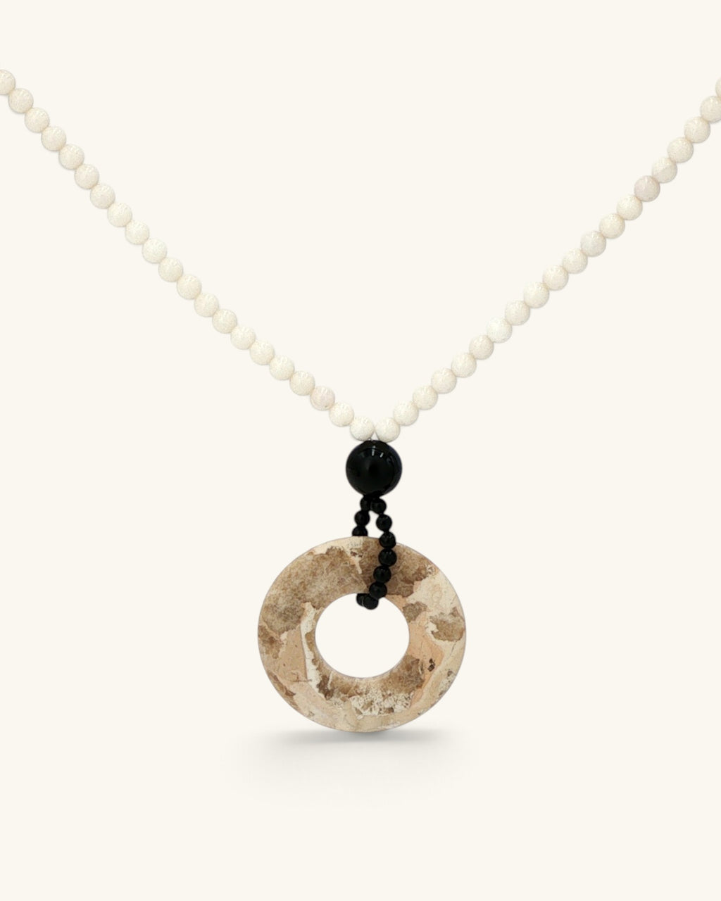 Close view of the brown jasper donut pendant below a black onyx bead and small black beads on mother of pearl