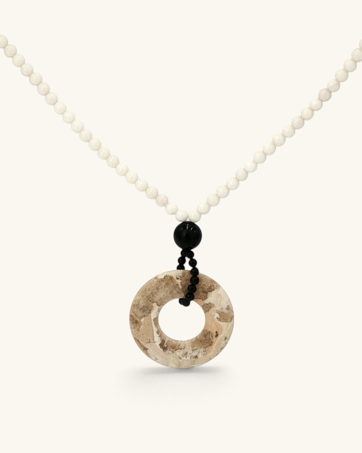 Close view of the brown jasper donut pendant below a black onyx bead and small black beads on mother of pearl