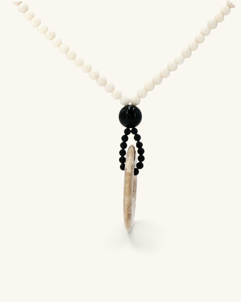Side view of the brown jasper donut pendant hanging edge-on from black beads on the mother of pearl strand