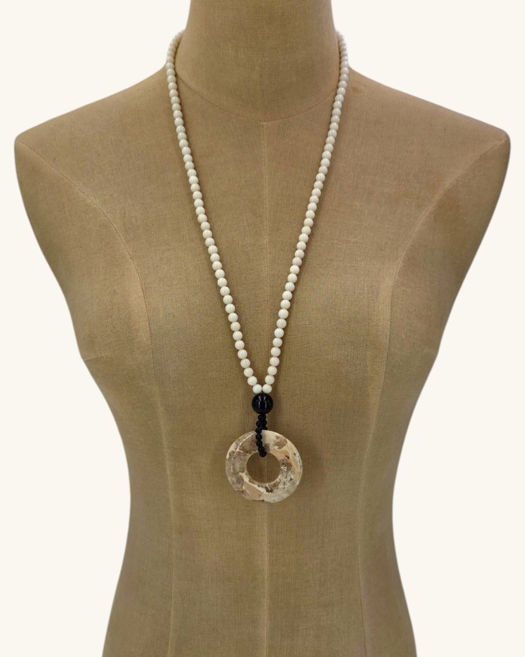 Mother of pearl bead necklace with brown jasper donut pendant shown long on a linen dress form