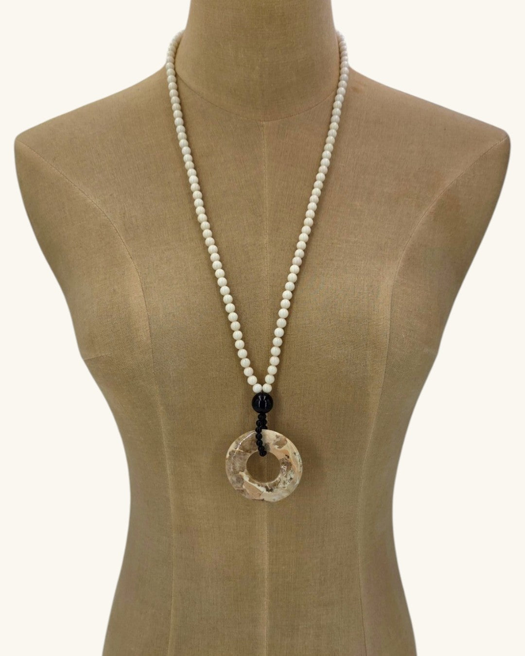 Mother of pearl bead necklace with brown jasper donut pendant shown long on a linen dress form