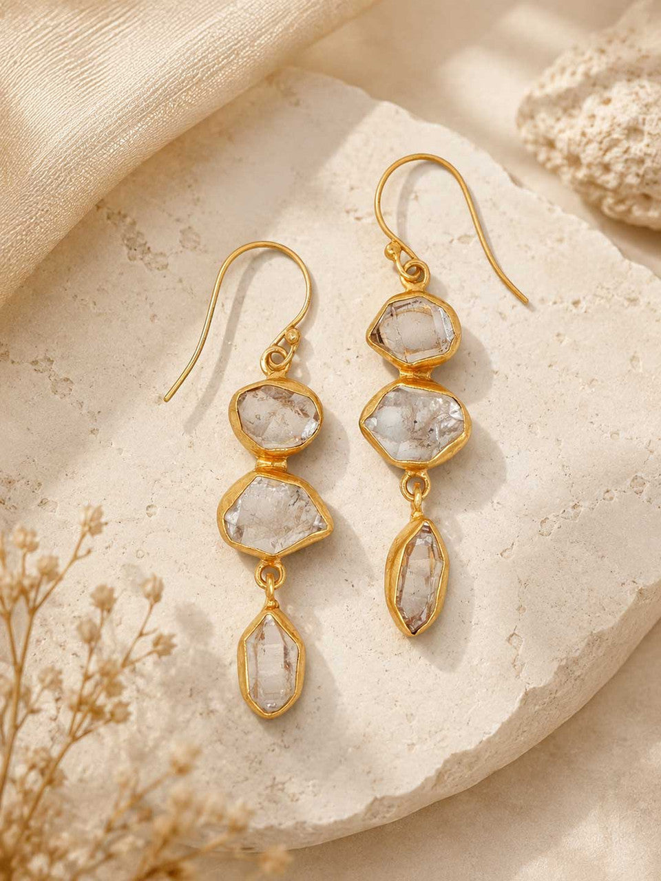 Triple Herkimer quartz gold-plated drop earrings laid on a stone surface with dried flowers, styled lifestyle view