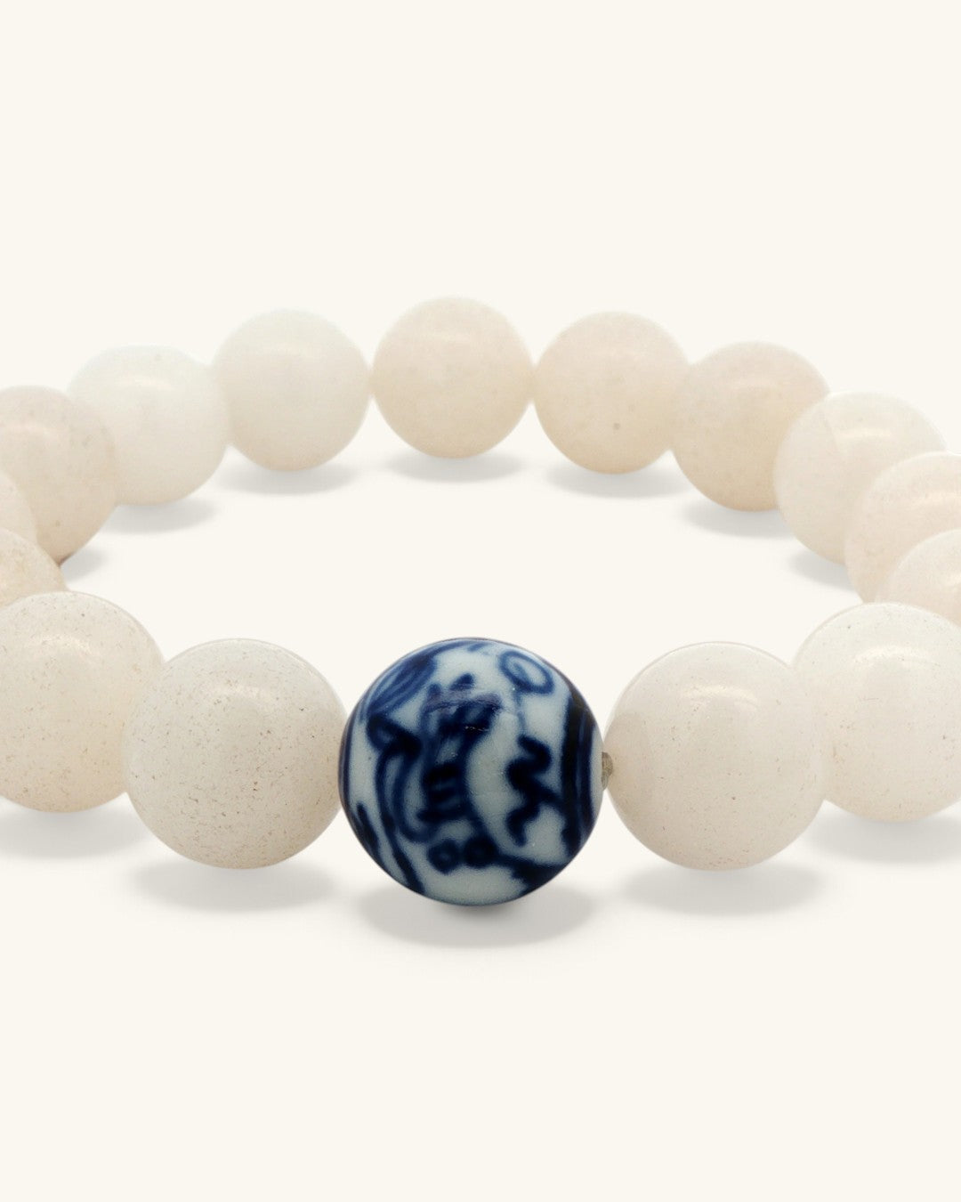 Close view of the cobalt blue painted porcelain bead between milky white jade beads on the stretch bracelet