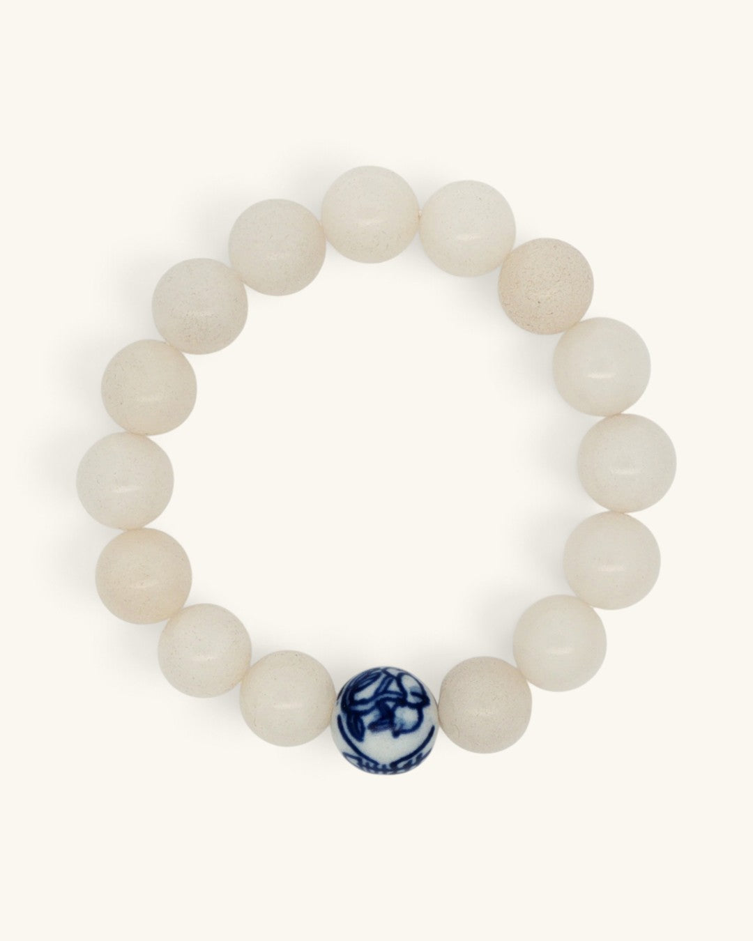 White jade bead bracelet laid flat in a circle, the blue and white porcelain bead at the bottom edge
