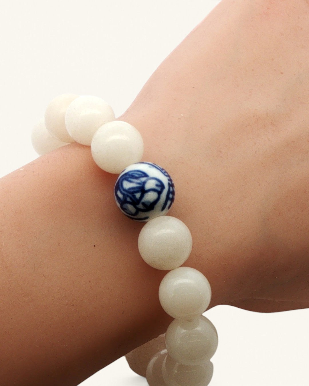 White jade bead bracelet with one blue and white porcelain bead, worn on a wrist, seen from above