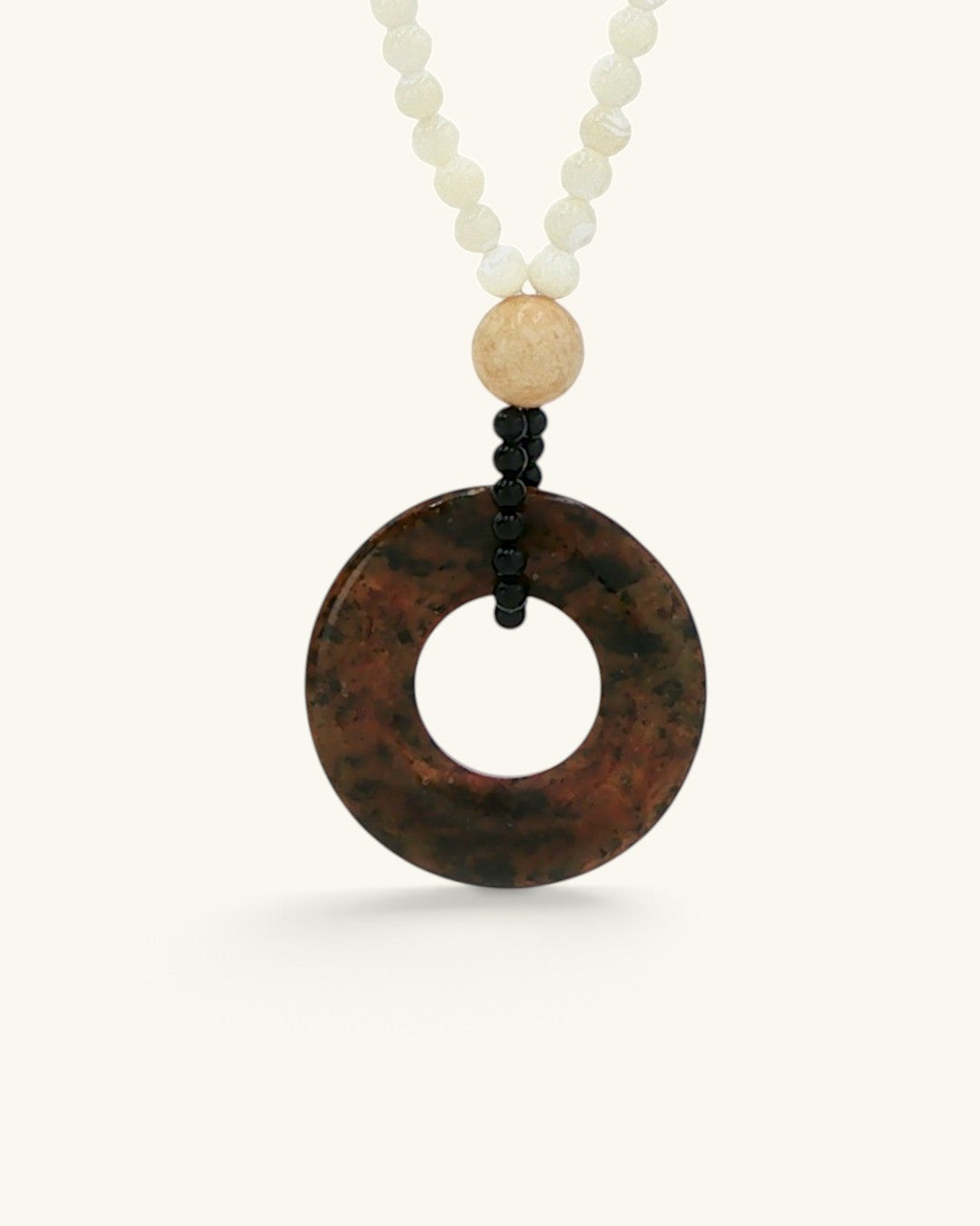Close view of the mottled brown and black riverstone donut pendant on small black beads below a tan stone bead